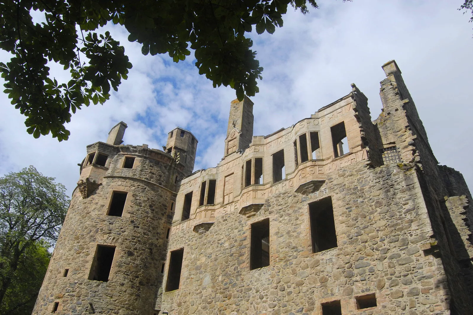 The roofless stone ruin of Huntly Castle seen from below, with a round tower at left and carved lettering along the upper wall.