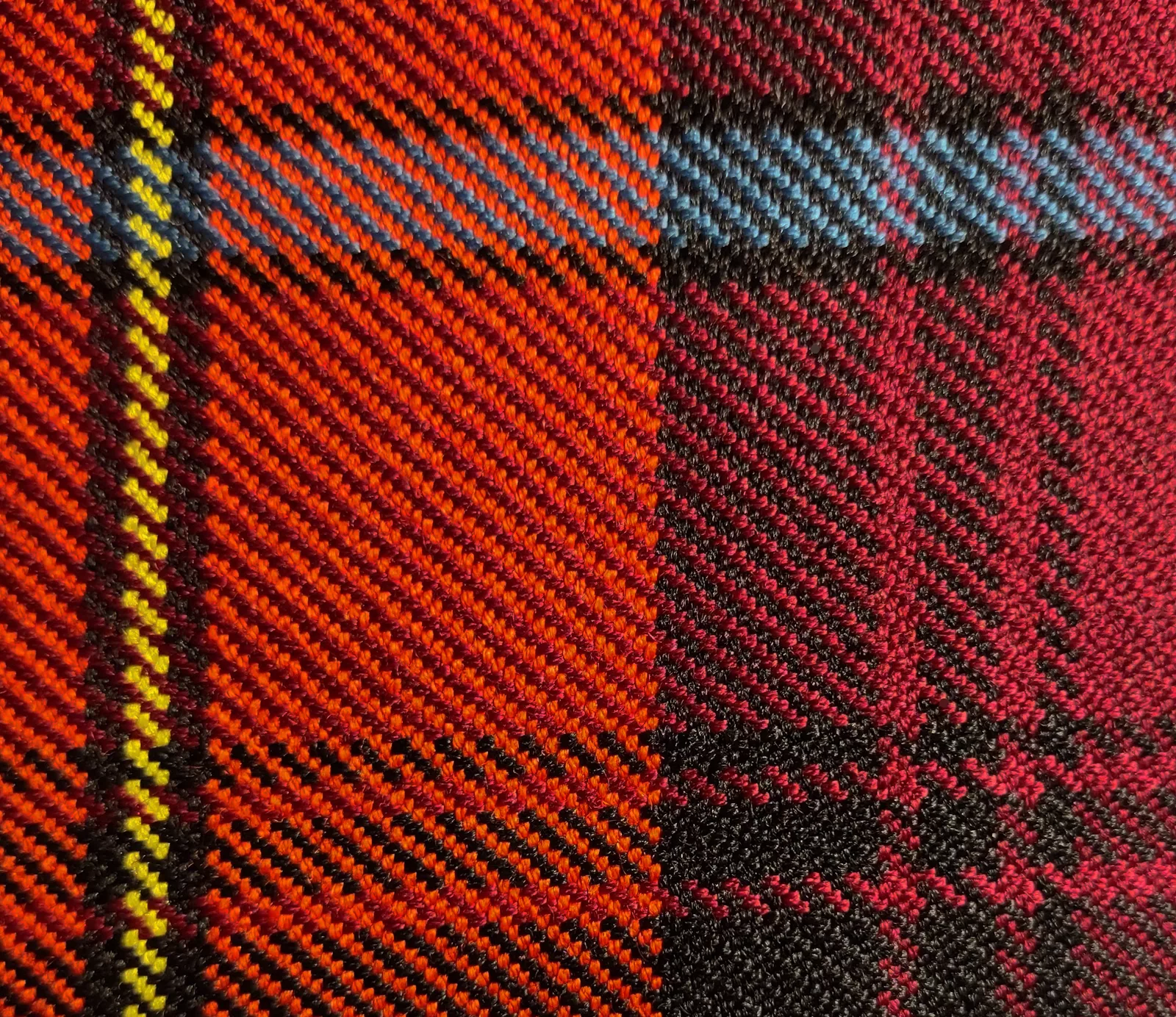 Close-up of woven tartan cloth in red, black, blue and yellow, showing the diagonal twill ribs of the weave